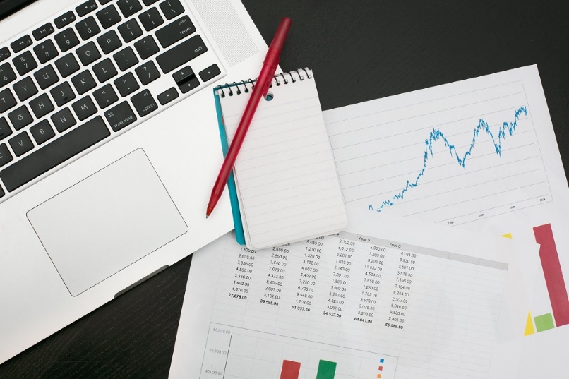 A laptop, notepad, pen, and documents with graphs and data analysis on a desk