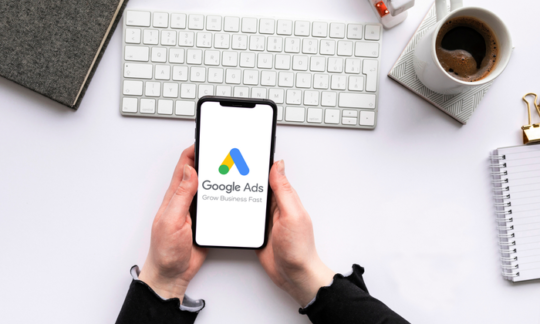 phone in hands with google ads opened, a cup of coffee, keyboard on table