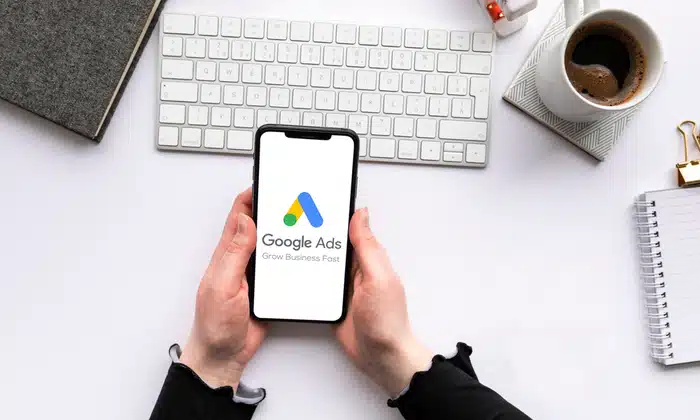phone in hands with google ads opened, a cup of coffee, keyboard on table