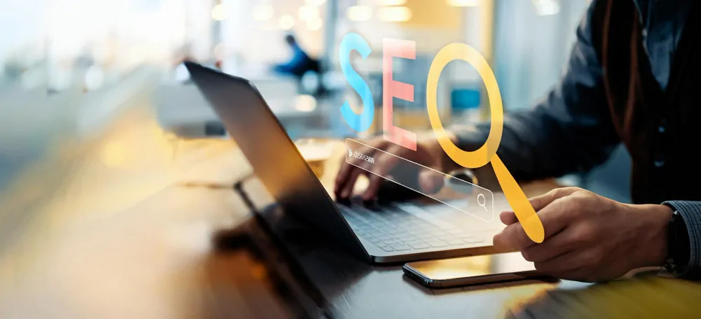 A person working on a laptop with a digital magnifying glass highlighting the word SEO, symbolizing SEO research or optimization.