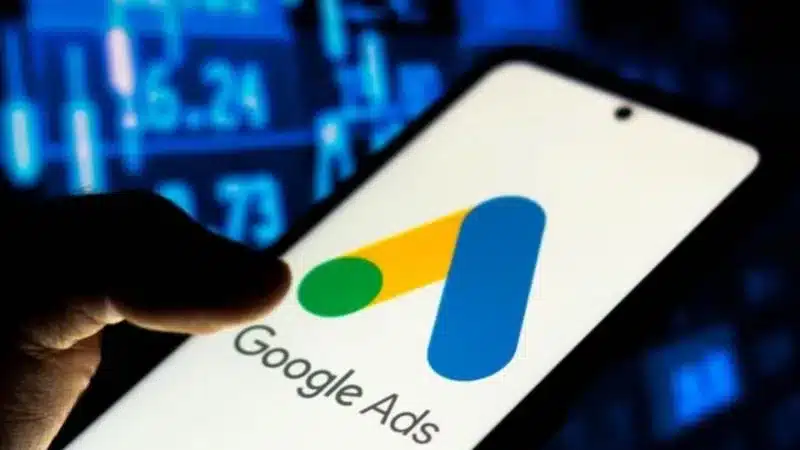 Close-up of a hand holding a phone displaying the Google Ads logo with a digital background.