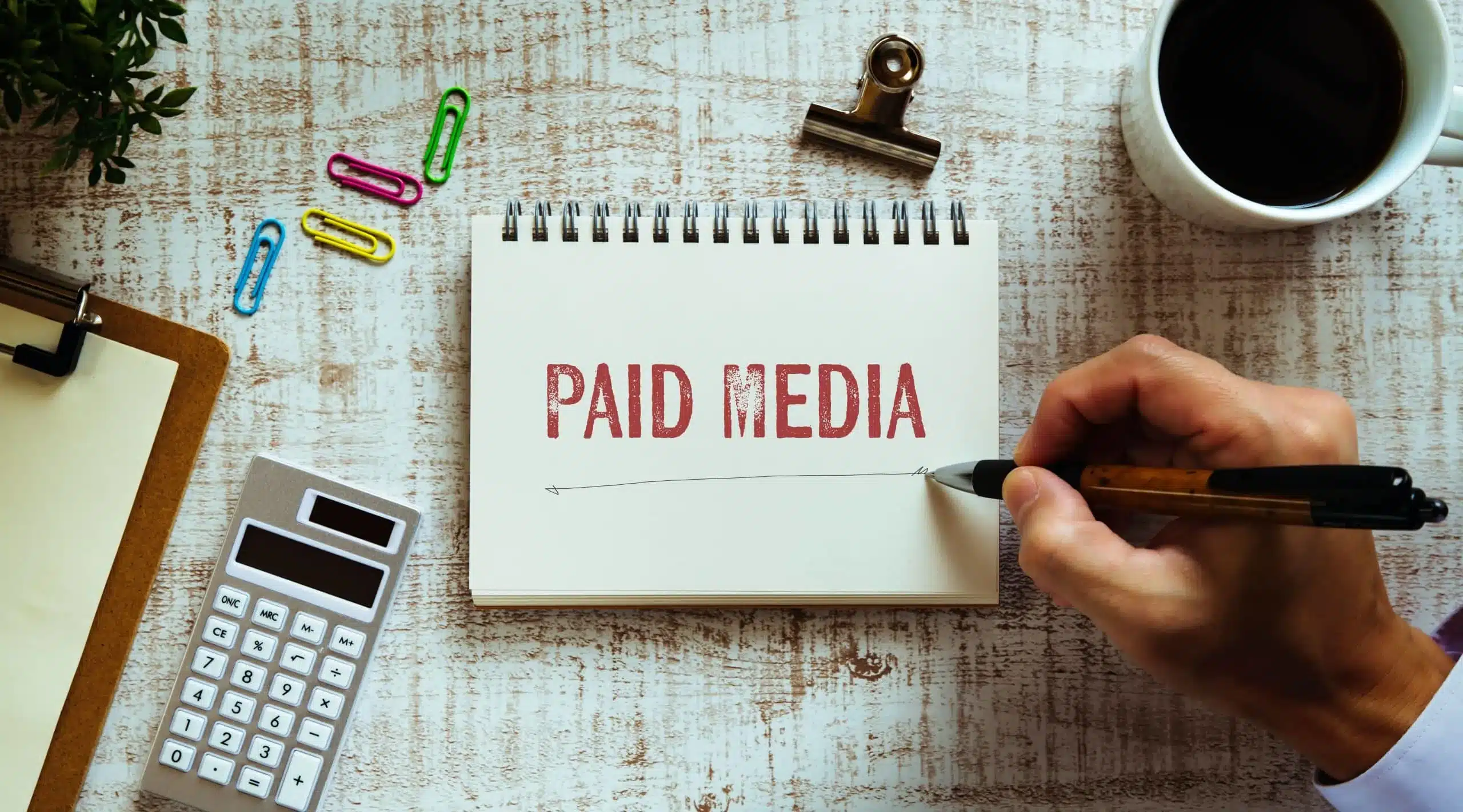 close up of hand writing paid media on a notepad