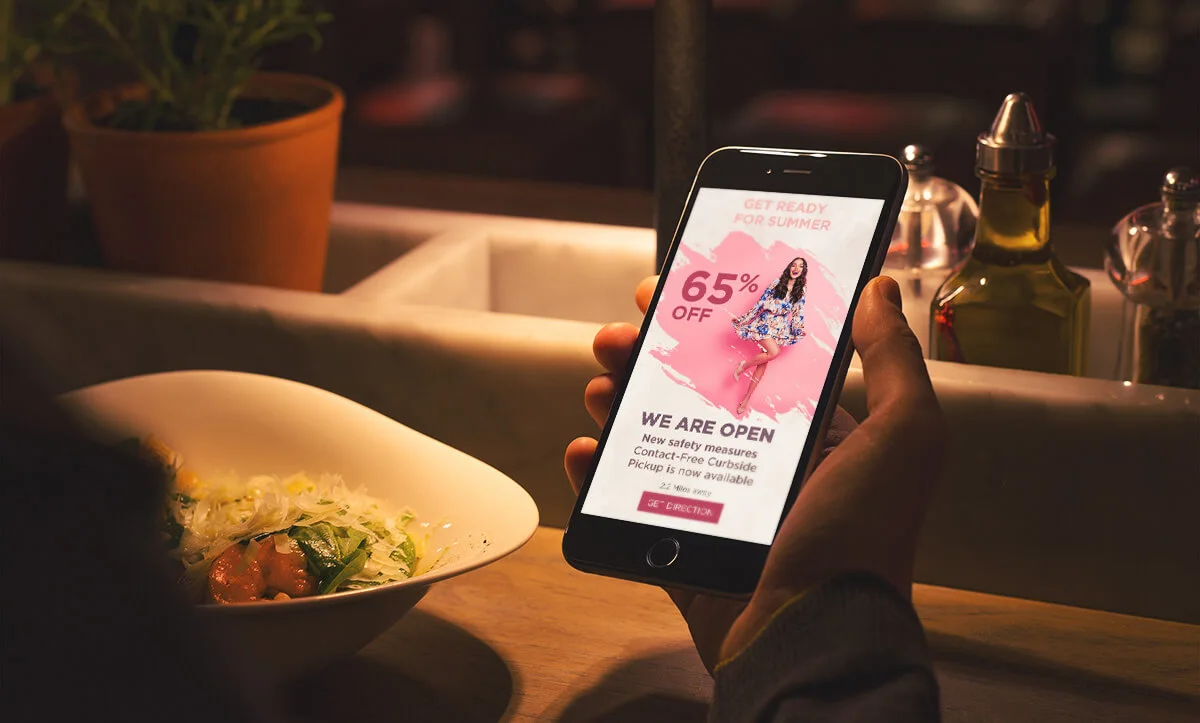Hand holding a smartphone showing a summer sale advertisement while dining at a restaurant. Hand holding a smartphone showing a summer sale advertisement while dining at a restaurant.