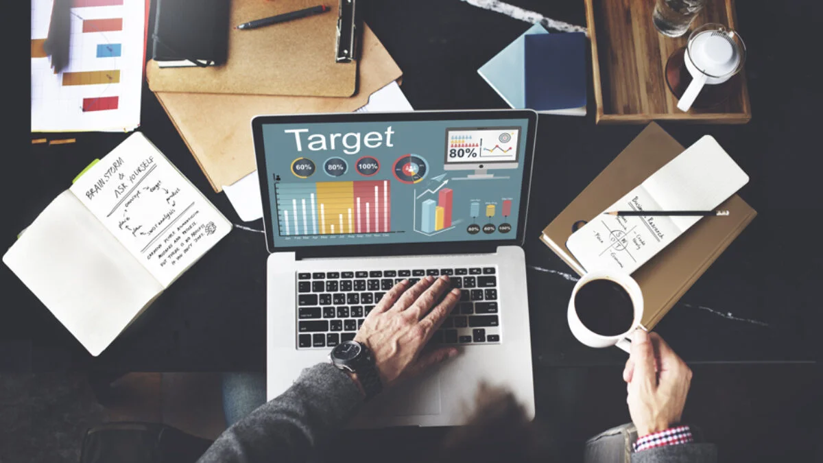 Person working on a laptop showing analytics dashboard with charts on a desk with coffee and notebooks.