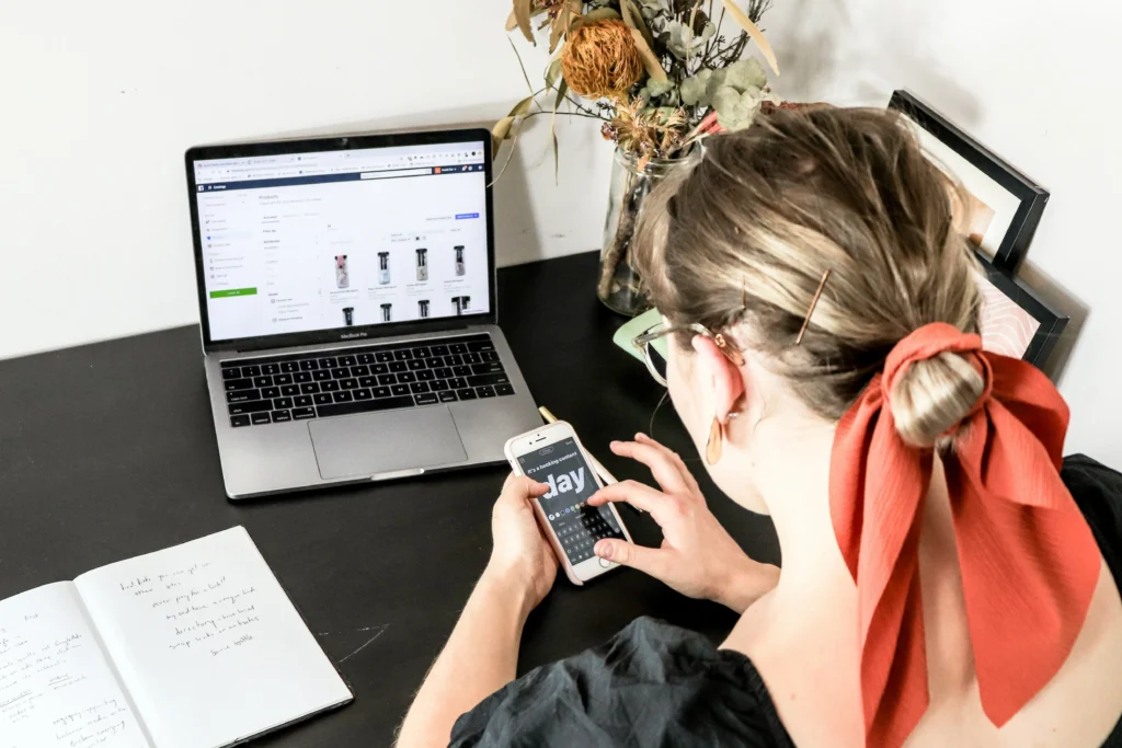 Woman browsing an ecommerce site on a phone while working on a laptop.