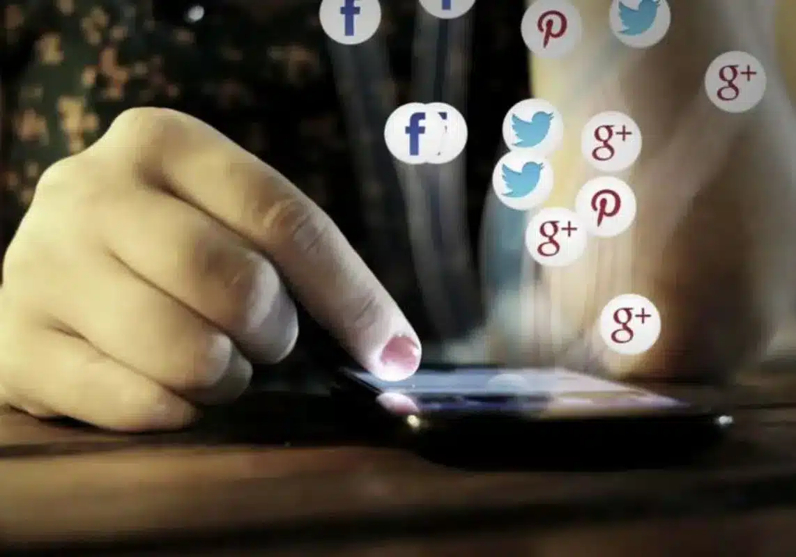 Hand using a smartphone with floating social media icons.