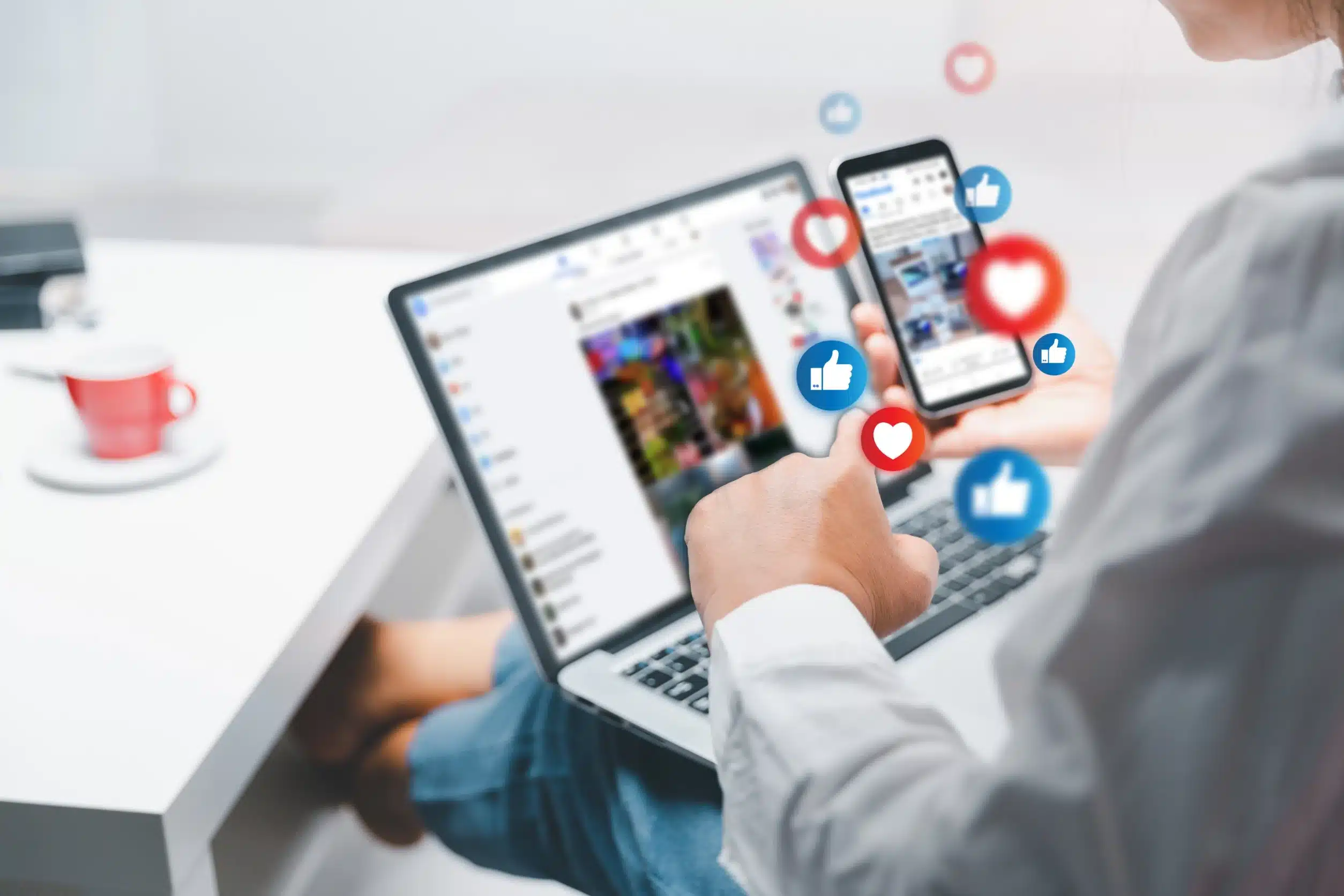 Person using a smartphone and laptop with social media engagement icons.